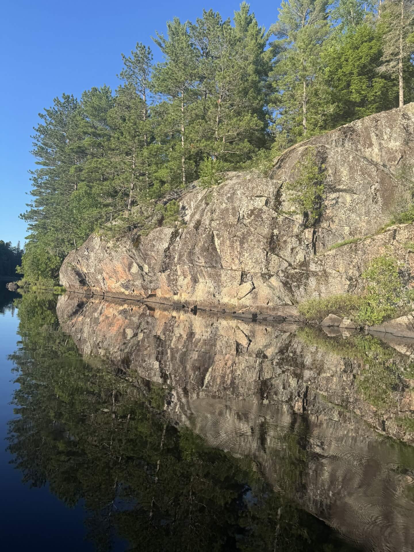 Rock cliff reflected in calm lake water at Craig Lake