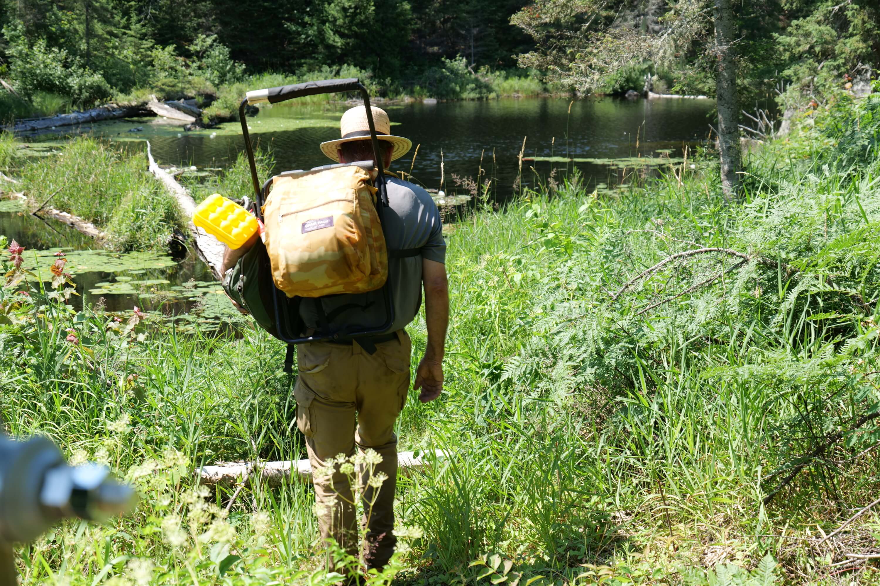 Hiker carrying a full backpack walking toward a backcountry lake
